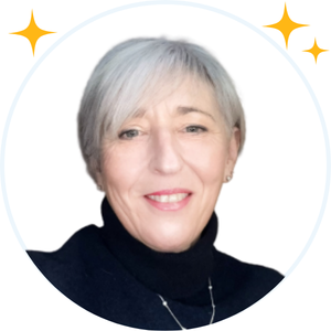 A grey haired lady in a dark blue polo jumper is smiling at the camera.